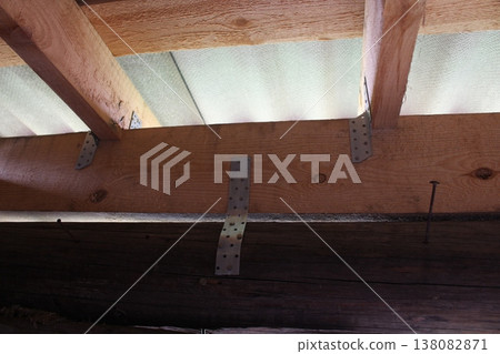 Building framework showing timber beams connected with perforated metal plates, corrugated roofing material overhead Building framework showing timber beams connected with perforated metal plates, corrugated roofing material overhead 138082871