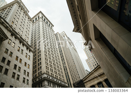 Historic high-rise buildings tower above Wall Street in Manhattan financial district. The narrow urban canyon reflects corporate finance, banking, and business activity in New York City. Historic high-rise buildings tower above Wall Street in Manhattan financial district. The narrow urban canyon reflects corporate finance, banking, and business activity in New York City. 138083364
