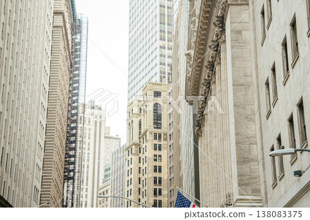 Tall skyscrapers and classic financial architecture rise above Wall Street in New York City. The financial district showcases corporate buildings, investment offices, and urban city infrastructure. 138083375