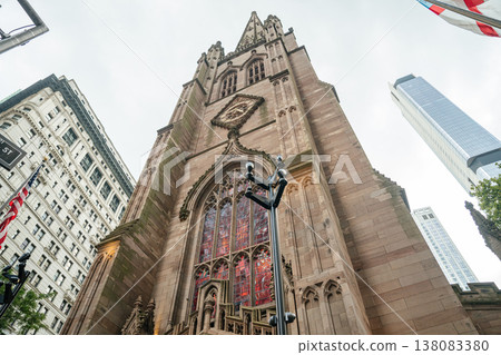 A close up view shows the Gothic church facade with stained glass windows in Manhattan New York. The historic stone tower stands tall among modern skyscrapers in the financial district. 138083380
