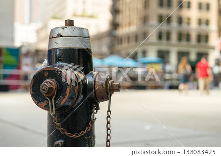 A black metal fire hydrant stands on a city sidewalk in New York with blurred pedestrians and buildings in the background. The urban street scene highlights public safety infrastructure in a busy A black metal fire hydrant stands on a city sidewalk in New York with blurred pedestrians and buildings in the background. The urban street scene highlights public safety infrastructure in a busy 138083425