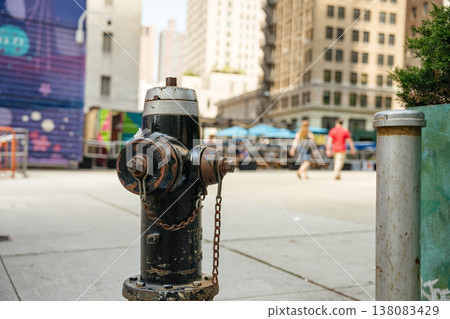 A black fire hydrant stands on a city sidewalk with blurred pedestrians and tall buildings in the background. The urban street scene reflects everyday life in downtown New York. A black fire hydrant stands on a city sidewalk with blurred pedestrians and tall buildings in the background. The urban street scene reflects everyday life in downtown New York. 138083429