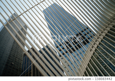A tall modern glass skyscraper rises into the sky framed by white architectural beams in New York City. The urban perspective highlights financial district architecture and contemporary city design. A tall modern glass skyscraper rises into the sky framed by white architectural beams in New York City. The urban perspective highlights financial district architecture and contemporary city design. 138083442