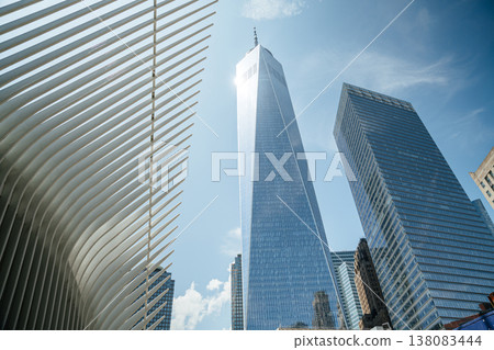 One World Trade Center rises high above downtown New York City next to the white Oculus structure. The glass skyscraper reflects sunlight against a clear blue summer sky. One World Trade Center rises high above downtown New York City next to the white Oculus structure. The glass skyscraper reflects sunlight against a clear blue summer sky. 138083444