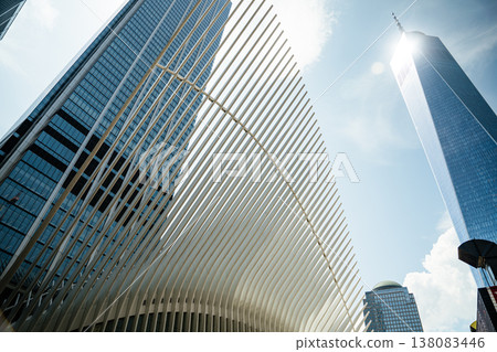 One World Trade Center rises high above the skyline of New York City next to the Oculus structure. The glass skyscraper reflects sunlight against a clear blue sky in Lower Manhattan. 138083446