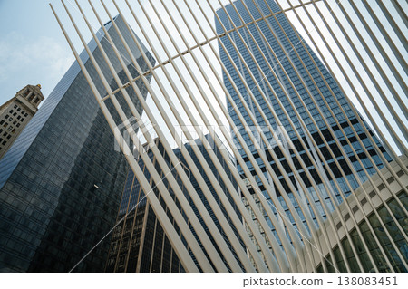 Modern glass skyscrapers rise behind the white ribbed structure of the Oculus in Lower Manhattan. The architectural lines create a dramatic perspective of the New York City skyline. Modern glass skyscrapers rise behind the white ribbed structure of the Oculus in Lower Manhattan. The architectural lines create a dramatic perspective of the New York City skyline. 138083451