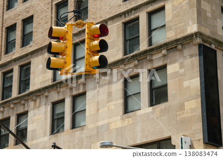 Hanging traffic signal over a Manhattan street with historic stone building in the background. The red light controls vehicle movement in a busy downtown intersection. 138083474