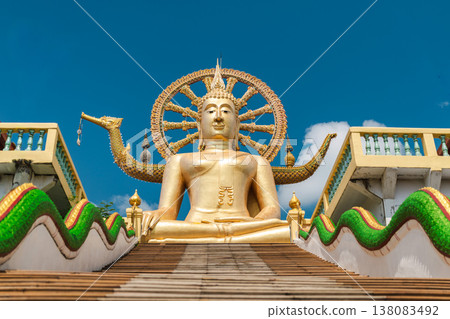 Majestic golden Buddha statue at Thai temple with long staircase and decorative serpents under blue sky 138083492