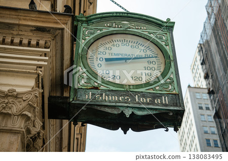 Ornate vintage thermometer sign mounted on a historic downtown building surrounded by tall city skyscrapers. The large temperature display highlights urban weather conditions in a busy metropolitan Ornate vintage thermometer sign mounted on a historic downtown building surrounded by tall city skyscrapers. The large temperature display highlights urban weather conditions in a busy metropolitan 138083495
