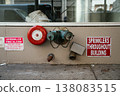 A red sprinkler fire alarm and standpipe connection are mounted on a building wall in New York City. Safety signage highlights fire protection infrastructure in an urban environment. 138083515