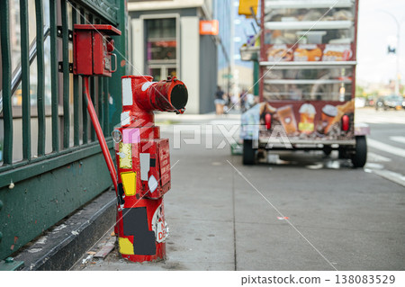 A red fire hydrant stands on a New York City sidewalk near a subway entrance and urban buildings. A street food truck and city traffic are visible in the background creating a busy metropolitan A red fire hydrant stands on a New York City sidewalk near a subway entrance and urban buildings. A street food truck and city traffic are visible in the background creating a busy metropolitan 138083529
