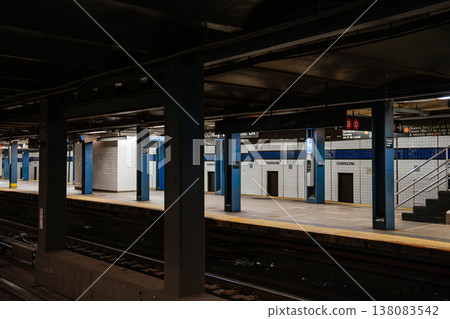 Wide view of Broadway Lafayette Street subway station platform in New York City. Underground metro scene with tiled walls, railway tracks, blue steel columns, and yellow safety edge. Wide view of Broadway Lafayette Street subway station platform in New York City. Underground metro scene with tiled walls, railway tracks, blue steel columns, and yellow safety edge. 138083542