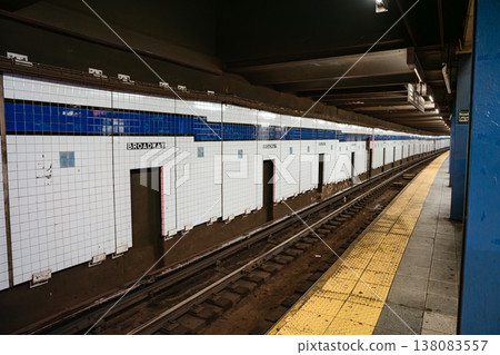 Broadway tiled wall and railway tracks inside Broadway Lafayette Street subway station in New York City. Underground metro platform with yellow safety edge and urban transit infrastructure. Broadway tiled wall and railway tracks inside Broadway Lafayette Street subway station in New York City. Underground metro platform with yellow safety edge and urban transit infrastructure. 138083557