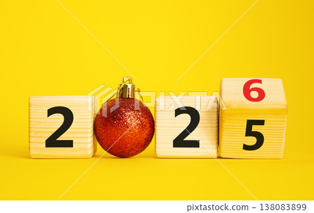 2026 New Year symbol. Businessman turns wooden cube and changes Year 2025 to 2026. Beautiful yellow background with Christmas ball. Copy space. Business and 2026 happy new year concept 138083899