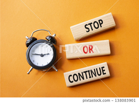 Stop or Continue symbol. Concept words Stop or Continue on wooden blocks. Beautiful orange background with alarm clock. Business concept and Stop or Continue. Copy space. 138083901
