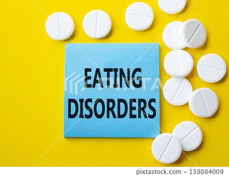 Eating Disorders symbol. Concept word Eating Disorders on blue note. Beautiful yellow background with pills. Medicine and Eating Disorders concept. Copy space Eating Disorders symbol. Concept word Eating Disorders on blue note. Beautiful yellow background with pills. Medicine and Eating Disorders concept. Copy space 138084009