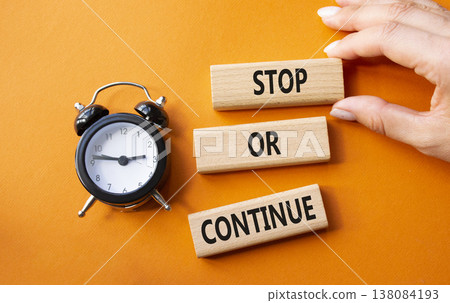 Stop or Continue symbol. Concept words Stop or Continue on wooden blocks. Businessman hand. Beautiful orange background with alarm clock. Business concept and Stop or Continue. Copy space. 138084193