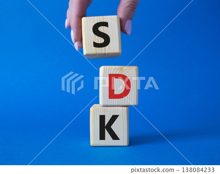 SDK - software development kit. Wooden cubes with word SDK . Businessman hand. Beautiful blue background. Business and software development kit concept. Copy space. 138084233