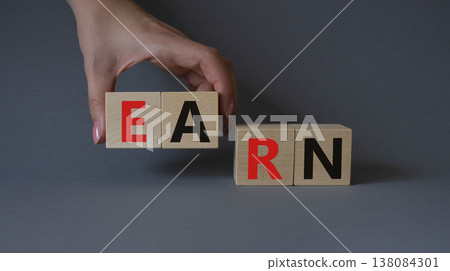 Earn symbol. Concept word Earn on wooden cubes. Businessman hand. Beautiful grey background. Business and Earn concept. Copy space. Earn symbol. Concept word Earn on wooden cubes. Businessman hand. Beautiful grey background. Business and Earn concept. Copy space. 138084301