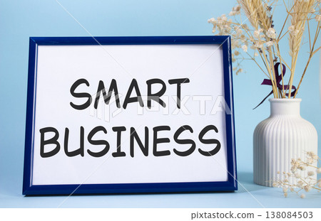 Smart business symbol. Concept words Smart business on beautiful wooden picture frame. Beautiful light blue background with flower vase. Business and Smart business concept. Copy space. Smart business symbol. Concept words Smart business on beautiful wooden picture frame. Beautiful light blue background with flower vase. Business and Smart business concept. Copy space. 138084503