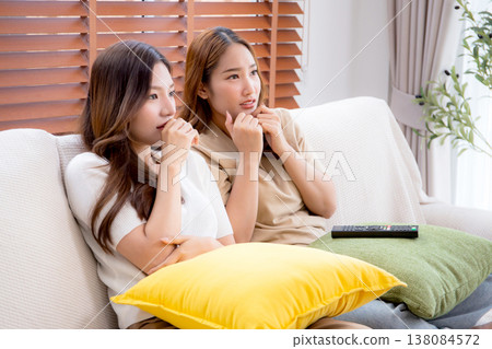 Happy young asian woman and friend watching television together with feeling scared afraid. Happy young asian woman and friend watching television together with feeling scared afraid. 138084572