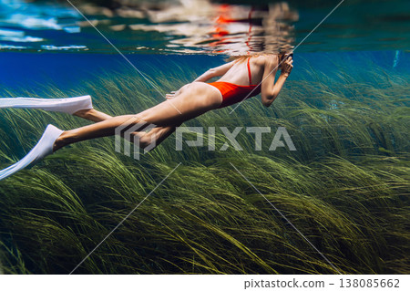 Woman swims underwater over algae at the bottom in freshwater lake. Freediving in crystal lake Woman swims underwater over algae at the bottom in freshwater lake. Freediving in crystal lake 138085662