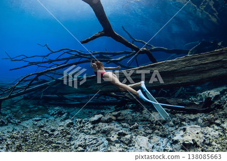 Freediver woman dives on deep in freshwater lake with sunken logs. 138085663