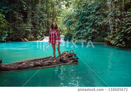 Woman on log in turquoise waterfall pool deep in tropical rainforest landscape Woman on log in turquoise waterfall pool deep in tropical rainforest landscape 138085672