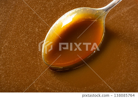 Caramel sauce in a spoon close-up, liquid caramel texture, sweet topping. Caramel sauce in a spoon close-up, liquid caramel texture, sweet topping. 138085764