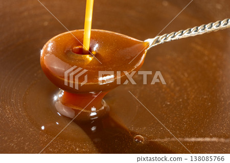 Liquid caramel sauce dripping from silver spoon. Liquid caramel sauce dripping from silver spoon. 138085766