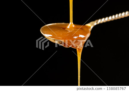 Sweet caramel sauce dripping from spoon, liquid caramel close-up. 138085767