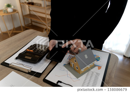 Young business woman is standing pressing calculator with house model Young business woman is standing pressing calculator with house model 138086679