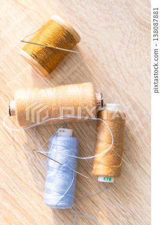 Colorful thread spools and sewing needles lying on a wooden surface, representing craft, hobby, and textile work 138087881
