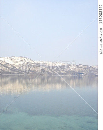 Lake Towada in winter: A breathtaking view of snow-covered mountains and the mirror-like surface of the lake. 138088522