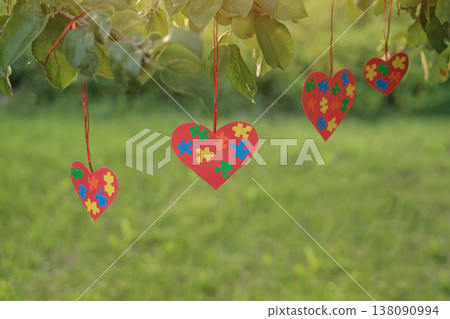 Suspended postcards in the shape of hearts, decorated with pieces of multicolored puzzles on a natural background. Autism Day Greeting Card Suspended postcards in the shape of hearts, decorated with pieces of multicolored puzzles on a natural background. Autism Day Greeting Card 138090994