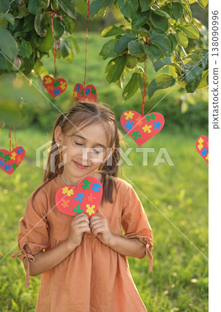 A gentle, sensual girl lovingly holds a heart-shaped postcard decorated with puzzles for autism Day 138090996