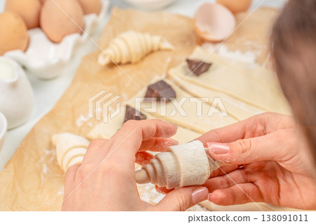 Hands shaping chocolate croissant from puff pastry dough, close-up bakery preparation process 138091011