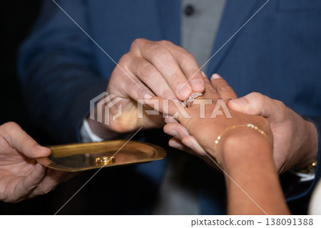 Groom placing wedding ring on bride's finger during ceremony vows in a church Groom placing wedding ring on bride's finger during ceremony vows in a church 138091388