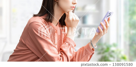 A woman/businesswoman thinking while looking at her smartphone 138091580