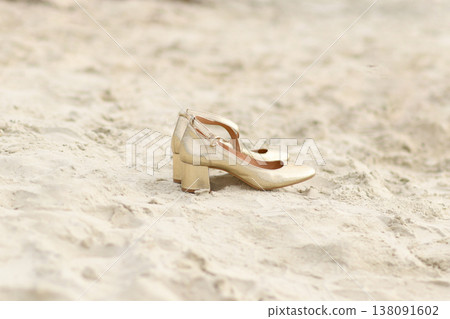 Golden block heel bridal shoes resting alone on beach sand 138091602