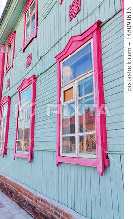 Row of vintage wooden house windows with vivid pink frames on a turquoise painted wall. The colorful architectural composition highlights traditional craftsmanship and charming historic building style 138091616