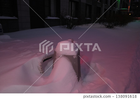 Street infrastructure buried in deep snow near residential buildings during winter evening snowfall. The dark urban landscape reflects harsh weather, seasonal climate and winter conditions in the city Street infrastructure buried in deep snow near residential buildings during winter evening snowfall. The dark urban landscape reflects harsh weather, seasonal climate and winter conditions in the city 138091618