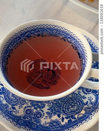 Herbal tea in a blue patterned cup with pastry and cream on a marble table. Cafe dessert pause, afternoon refreshment, sweet serving, and tabletop hospitality detail in soft daylight 138091638