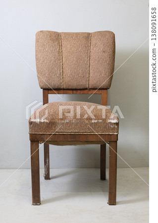 Vintage brown chair stands alone against a simple white wall, inviting nostalgia and comfort for anyone who sits upon it Vintage brown chair stands alone against a simple white wall, inviting nostalgia and comfort for anyone who sits upon it 138091658