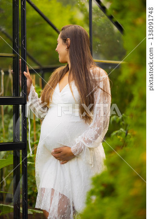 Pregnant woman in a greenhouse wearing a white lace dress 138091748