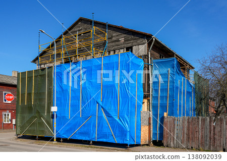 Old wooden house under renovation with scaffolding and blue protective cover on urban street 138092039