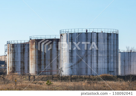 Large industrial storage tanks with rust stains in open landscape under clear blue sky 138092041