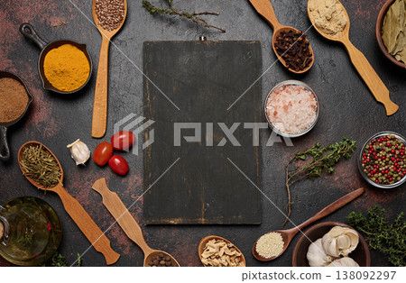 A cutting board is surrounded by spices turmeric, cloves, pepper, salt, sesame seeds, flax, and ginger A cutting board is surrounded by spices turmeric, cloves, pepper, salt, sesame seeds, flax, and ginger 138092297