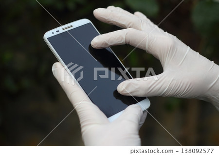closeup of a young man wearing latex gloves while is using his smartphone 138092577