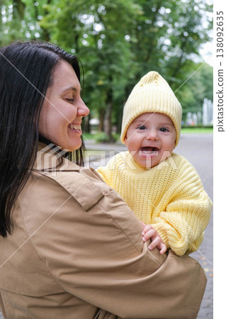 Mother Holding Baby in Yellow Outfit at Park Mother Holding Baby in Yellow Outfit at Park 138092635